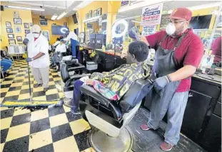  ?? JOE BURBANK/ORLANDO SENTINEL ?? Barber Leroy Owens, right, cuts a customer’s hair at J Henry’s Barber Shop on Church Street. J Henry’s was one of the hair salons that reopened Monday as a part of the state’s coronaviru­s plan.