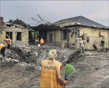  ?? A WORKER David Goldman Associated Press ?? arrives with a broom at a crater caused by a rocket strike Friday on a house in Kramatorsk, Ukraine. No injuries were reported. One Russian attack in the city killed three people, the mayor said.