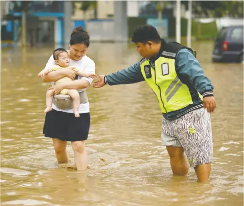  ?? NOEL CELIS / AFP VIA GETTY IMAGES ?? People wade down a flooded street following a heavy rain on Thursday in Zhengzhou, in China’s Henan province.