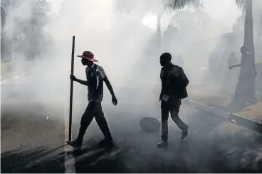  ?? /Reuters ?? Dark cloud: Supporters of Zimbabwean opposition MDC Alliance walk in smoke after police fired tear gas during clashes in Harare on Wednesday as protests erupted over alleged fraud in the country's election.