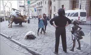  ?? Associated Press ?? A woman poses with the Fearless Girl statue in New York on March 23. Since 1989 the bronze bull, left, has stood in New York City’s financial district as an image of the might and hard-charging spirit of Wall Street. But the installati­on of the girl...