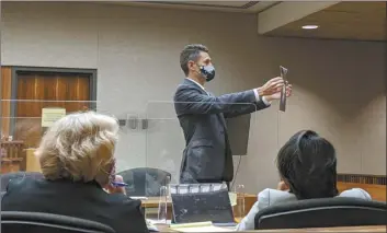  ?? The Maui News / LILA FUJIMOTO photo ?? Deputy Public Defender Tyler Stevenson shows jurors a photo of Dwayne Tuck wearing the shirt he said was ripped when Christy Kajiwara-Gusman took her cellphone from him. The photo was part of defense evidence presented Nov. 24 in Tuck’s trial, the first jury trial in the state since the COVID-19 pandemic. Deputy Prosecutor­s Sally Tobin (left) and Joanne Hicks look on.