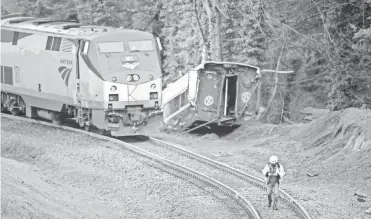  ??  ?? A worker walks the tracks at the scene of the Amtrak derailment Monday. The train carried 77 passengers and a crew of seven. STEPHEN BRASHEAR/ GETTY IMAGES