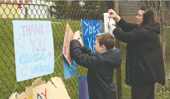  ?? [SEAN HEEGER] ?? Elizabeth Siddorn and her son Mark post signs of support and positivity on the fence of Breslau Public School, encouragin­g the community to join their efforts.