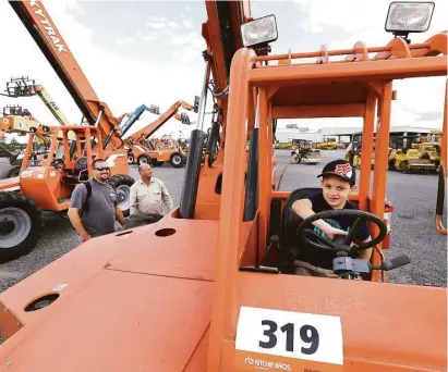  ?? Melissa Phillip / Houston Chronicle ?? Clayton Hartman, 8, of Magnolia sits in the driver’s seat of a lift as his dad, Joe Hartman, left, and George Hosford look at equipment during an auction this month at the Humble-area location of Ritchie Bros.