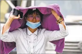  ?? ANDY WONG Associated Press ?? A WOMAN uses a sweater as a sun shield on a hot day in Beijing on Monday.