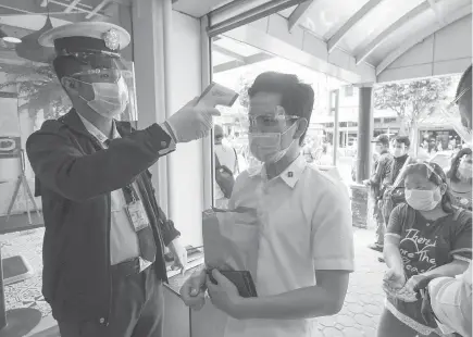  ?? Photo by Jean Nicole Cortes ?? EQUIPPED. A guard checks the temperatur­e of a mall goer before allowing entry. Establishm­ents in the city strictly implement the “No Face Mask, No Face Shield, No Entry” policy.