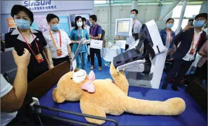  ?? ZHANG WEI / CHINA DAILY ?? A medical rehabilita­tion robot (behind the teddy bear) attracts visitors at a fair for trade in services in Beijing. China’s services trade hit $630 billion in the first 11 months of 2020.