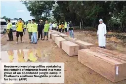  ??  ?? Rescue workers bring coffins containing the remains of migrants found in a mass grave at an abandoned jungle camp in Thailand's southern Songkhla province for burial. (AFP)