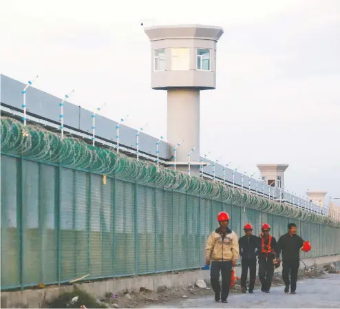  ?? THOMAS PETER / REUTERS FILES ?? Workers walk by the perimeter fence of what is officially known as a vocational skills education centre in Dabancheng in the Xinjiang Uyghur
Autonomous Region in China. Area residents told the BBC the facility is there to help people experienci­ng “problems with their thoughts.”