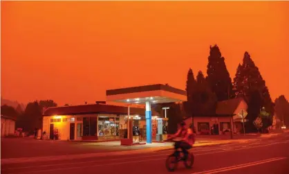  ?? Photograph: Josh Edelson/AFP/Getty Images ?? A man rides his bike past a gas station as smoke fills the sky in Greenville, California last week. The Dixie fire has become the largest in California after it exploded in size over the weekend.