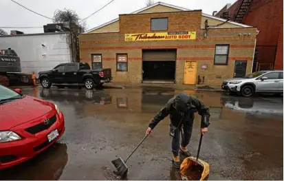  ?? PHOTOS BY DAVID L. RYAN/GLOBE STAFF ?? A man from the Thibedeau Auto Body garage swept up the front street where a nearby shooting occurred at 10 Camden St. in Lynn last night.