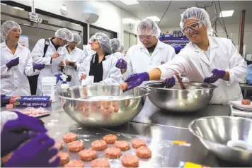  ?? Gabrielle Lurie / The Chronicle ?? Kevin Hong (right) throws a ball of plant-based meat into a bowl in the Impossible Foods kitchen.