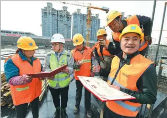  ?? CHENG GONG / FOR CHINA DAILY ?? Huang Chunping (right) and Liu Tengteng (second from left), employees of China State Constructi­on Engineerin­g Corp who were named the Most Beautiful Workers in Beijing, share their awards with coworkers at a constructi­on site in the capital’s Tongzhou...