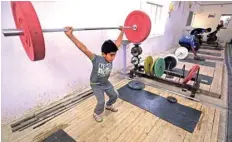  ??  ?? A boy lifts weights as he trains at the local weightlift­ing club in the town of Badra. — AFP