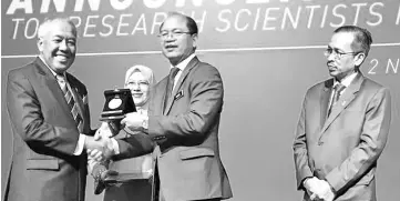  ??  ?? Tangau presenting the Senior Fellow Award to Ahmad Tajuddin (left) while Mosti secretary general Datuk Seri Dr Azhar Mohd Yahya (extreme right) looks on.