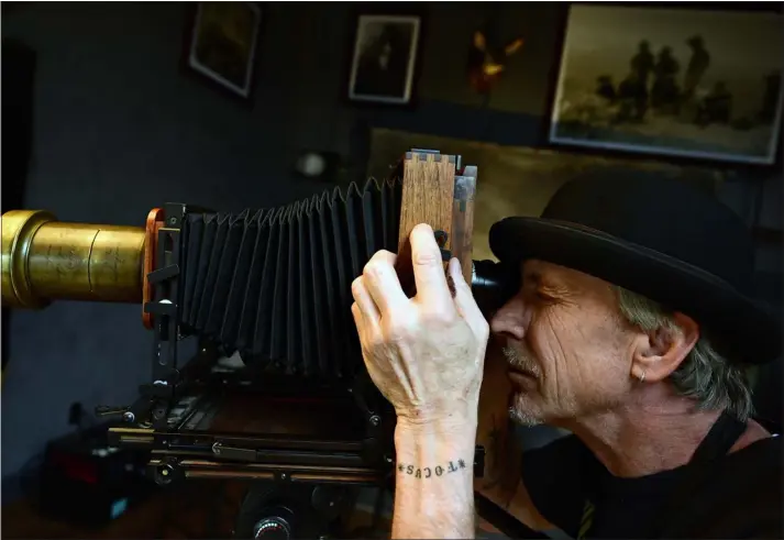  ?? PHOTOS BY HELEN H. RICHARDSON - THE DENVER POST) ?? Tintype photograph­er Tim Brown lines up a photograph in his wet plate camera for a photo by carefully looking through the back of it to focus the camera in his studio on March 20 in Salida, Colorado. When using these large cameras the image is upside down when viewed from the back of the camera making it more difficult to compose photograph­s. In order to see and focus the image, Brown will also use a black cloth to block out the light and a photograph­ic loupe to check on the sharpness of the image on the glass plate on the back.