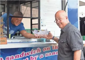  ?? FOOD NETWORK ?? Mike Stanley hands Andrew Zimmern his order from his food truck, Stanley’s Sweet Street Treats, as seen on Big Food Truck Tip, Season 1.