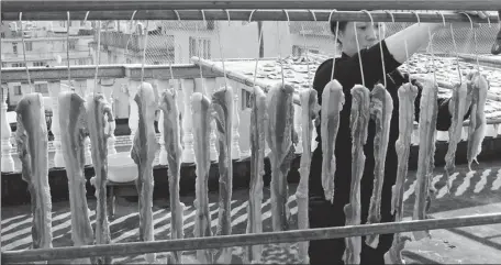  ?? CAI KUANYUAN / FOR CHINA DAILY ?? A woman in Wenzhou, Zhejiang province, hangs up cured meat to dry in the last month of the lunar calendar.