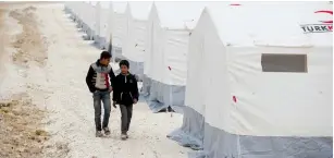  ?? (Reuters) ?? DISPLACED SYRIAN BOYS walk past tents supplied by the Turkish Red Crescent at Kelbit camp in Idlib province, near the Syrian-Turkish border this week.