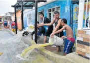  ??  ?? Varios jóvenes sacan el agua que inundó su casa durante el aguacero que cayó ayer en Barranquil­la.