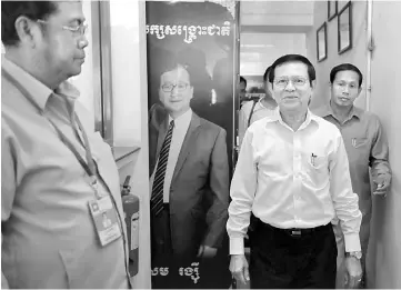  ??  ?? Cambodia’s opposition acting president Kem Sokha (second right) walks past a portrait of Sam, at the CNRP headquarte­rs in Phnom Penh. — AFP photo