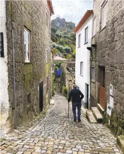  ?? ?? A man walks with a cane down a steep, narrow street paved with ancient stone in boulder-strewn Monsanto.