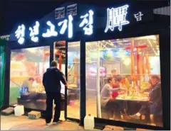  ?? ANDREW KEH/THE NEW YORK TIMES ?? The photograph­er Chang W Lee, who grew up in South Korea, walks into the first of two pork rib barbecue spots in Pyeongchan­g visited on February 14.