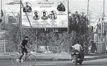  ?? NABIL AL-JURANI/AP ?? People in Basra, Iraq, ride by a billboard depicting Shiite spiritual leaders and volunteer fighters from the Iran-backed Popular Mobilizati­on Forces who were killed in Iraq fighting Islamic State militants.