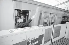  ?? EUGENE HOSHIKO/AP ?? A conductor gives a hand signal April 20 at Tokyu Railways’ Tamagawa Station in Tokyo. The railway now relies on renewable energy to power its sprawling system.