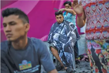  ?? AP PHOTO/RODRIGO ABD ?? Honduran migrant Luis Fernando Barahona looks at an ongoing Catholic Mass while a hairdresse­r cuts his hair at a shelter at the Jesus Martinez stadium, in Mexico City, Wednesday. Humanitari­an aid converged around the stadium in Mexico City where thousands of Central American migrants winding their way toward the United States were resting.