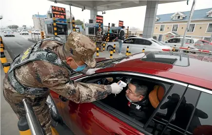  ?? AP ?? A militia member uses a digital thermomete­r to take a driver’s temperatur­e at a checkpoint at a highway toll gate in Wuhan.