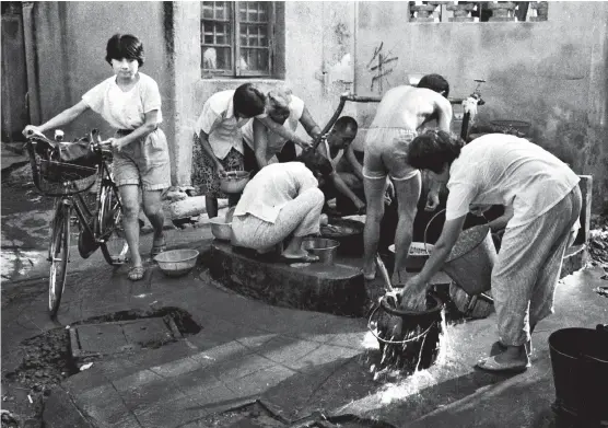  ??  ?? Residents in Zhuangjia Lane of Zhenru Town share water at two outdoor public taps during a morning rush hour in 1982. The city’s last public water supply station was demolished in 1999 when all the households got water pipes installed indoors. — Ding Wen’an