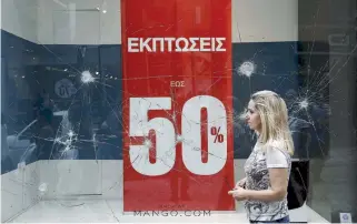  ??  ?? A woman passes a vandalized clothing store on Ermou Street in central Athens yesterday. A total of 67 downtown shops were damaged during rioting on Monday night, city Mayor Giorgos Kaminis said yesterday.