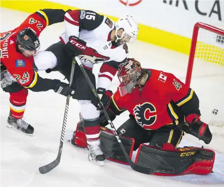  ?? PHOTOS: JIM WELLS ?? Flames defenceman Travis Hamonic hits Arizona Coyotes centre Brad Richardson as he crashes goalie Mike Smith in the Calgary net, but there was no rattling Smith Thursday night as he posted the shutout in a 3-0 contest at the Scotiabank Saddledome.