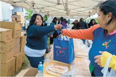  ?? JOSHUA BESSEX/AP ?? Yvonne King, left, hands out food to community members Tuesday near a Tops Friendly Market in Buffalo, New York.