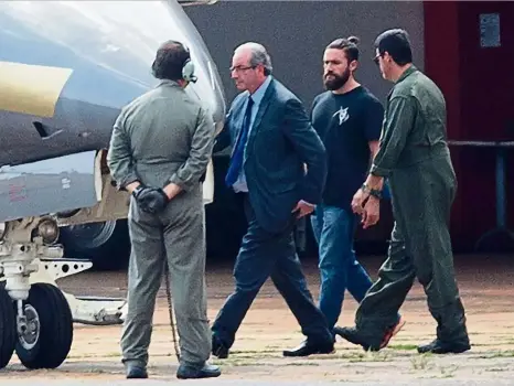  ?? — AFP ?? Under arrest: Cunha (in coat and tie) being escorted to a Federal Police plane in Brasilia.