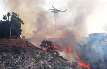  ?? REED SAXON / ASSOCIATED PRESS ?? A Los Angeles County Fire Department helicopter makes a water drop on flames sweeping up a steep canyon wall, threatenin­g homes on a ridge line after a wildfire swept through the Bel Air district of Los Angeles on Wednesday.