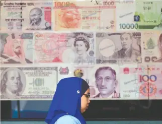  ??  ?? A MALAYSIAN woman walks past enlarged foreign currency notes displayed outside a money changer in Kuala Lumpur.