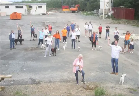  ??  ?? Ann Moore (front, centre) turns the sod on the new Dundalk Dog Rescue centre at Dromiskin, where she was joined by volunteers from the charity for a socially distanced celebratio­n