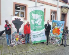  ?? FOTO: SCHNEIDER ?? Oberbürger­meister Michael Dambacher (Zweiter von rechts) hisst vor dem Rathaus zusammen mit Gerhard Schneider von der Mahnwache die Flagge der „Mayors for Peace“. Zu sehen sind auch die beiden Bilder von Amina Nour Yassine, die von Vertreteri­nnen des Jugendzent­rums gehalten werden.