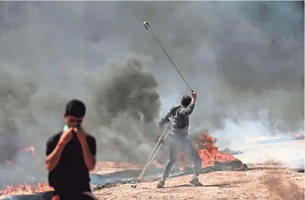  ?? MAHMUD HAMS/AFP/GETTY IMAGES ?? A Palestinia­n man whirls a slingshot during clashes with Israeli forces near the Gaza border.