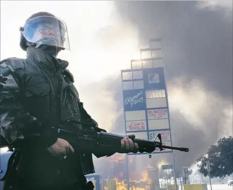  ?? David Butow Corbis via Getty Images ?? A MEMBER of the National Guard stands near a burning building during the frenzy of violence that swept Los Angeles 25 years ago.