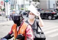  ?? — AFP photo ?? A woman is seen riding the back of a motorbike taxi shielding herself from the sun with paper during heatwave conditions in Bangkok. Last month was the warmest February on record globally according to Europe’s climate monitor.