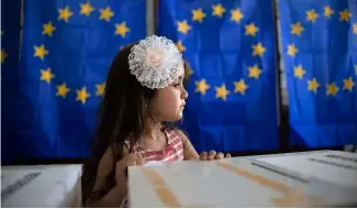  ?? ?? A little girl waits for her mother to vote, backdroppe­d by voting booths with curtains depicting the European Union flag in Baleni, Romania, in 2019.