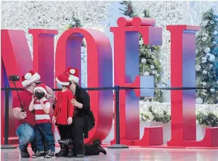  ?? GRAHAM HUGHES THE CANADIAN PRESS ?? People wear face masks as they pose next to a Christmas display in Montreal on Sunday.