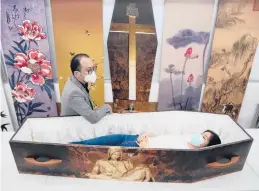  ?? KIN CHEUNG/AP ?? Wilson Tong, CEO of LifeArt Asia, stands near a live reporter in a cardboard coffin Friday at Tong’s factory in Hong Kong. Each coffin can hold up to 441 pounds.