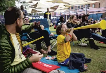  ?? Kent Nishimura Los Angeles Times ?? AMINA TAURAS, 4, blows a vuvuzela while her father, Mike Tauras, 37, left, watches at a World Cup party in L.A. In Mexico City, thousands of fans who had gathered at iconic locales celebrated a cathartic moment.