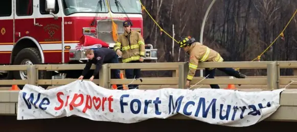  ?? TOPHER SEGUIN/REUTERS ?? Firefighte­rs adjust a sign above Memorial Dr. in Fort McMurray, Alta. Residents began returning home Wednesday and companies are resuming operations after the devastatin­g wildfire.