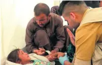  ?? Balint Szlanko / AP Photo ?? A man comforts his daughter as a doctor treats her for food poisoning in a camp east of Mosul yesterday.